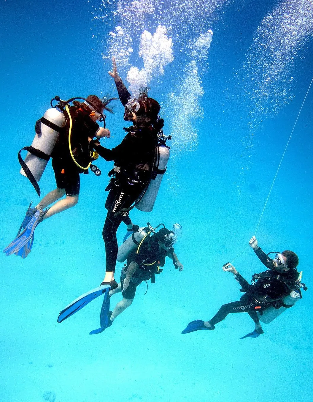 A scuba diving instructor ascending from a dive with his 3 students