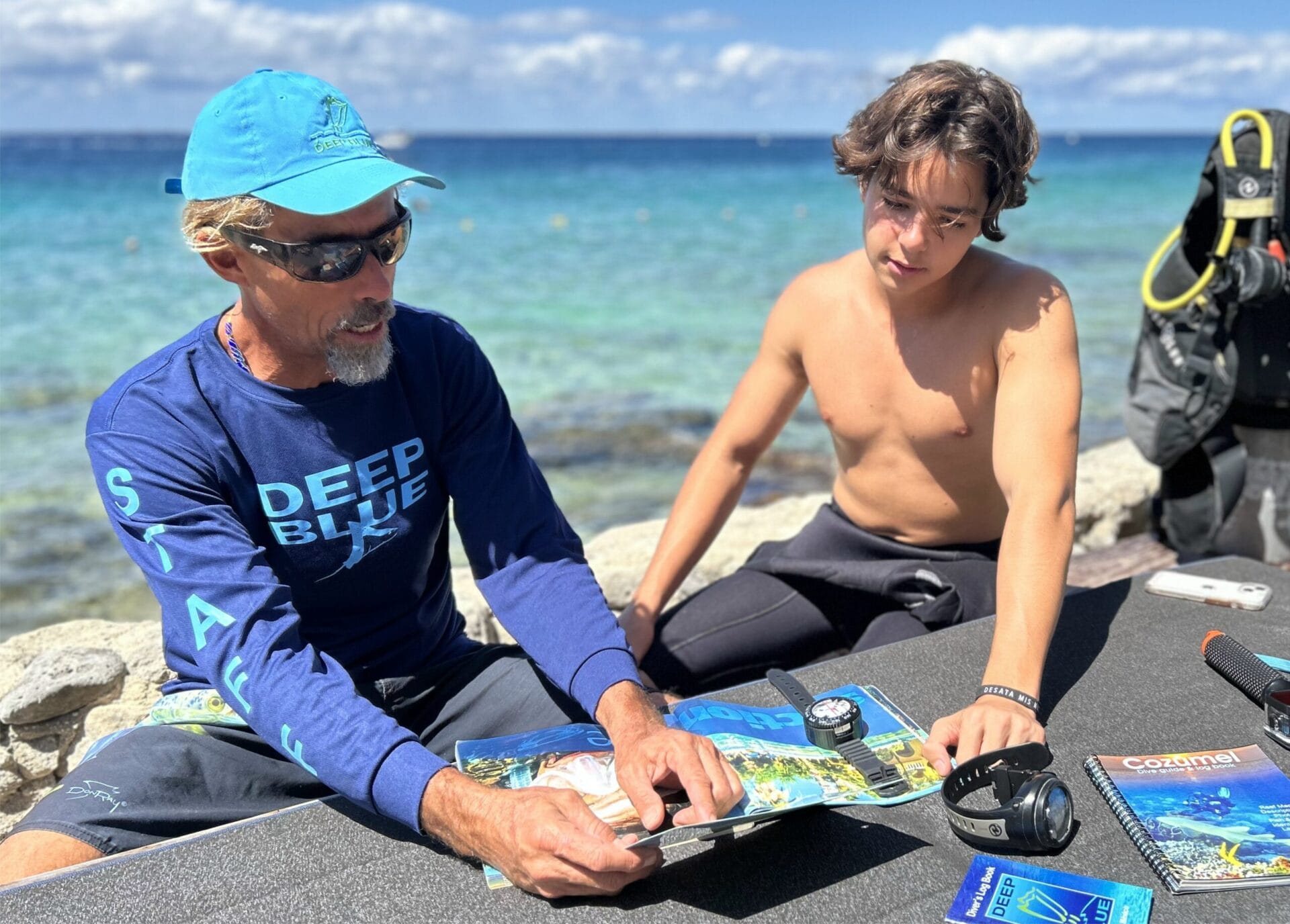 Diver instructing teenager on oceanic maps by the sea